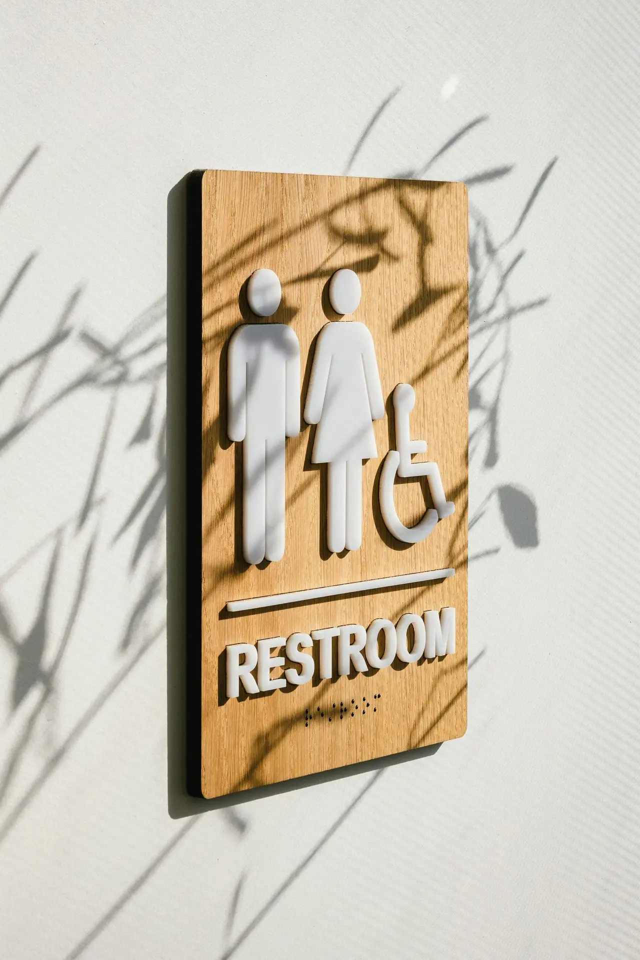 Wooden Restroom Sign with Accessibility Icons Wooden restroom sign featuring icons for male, female, and wheelchair accessibility, with braille underneath.
