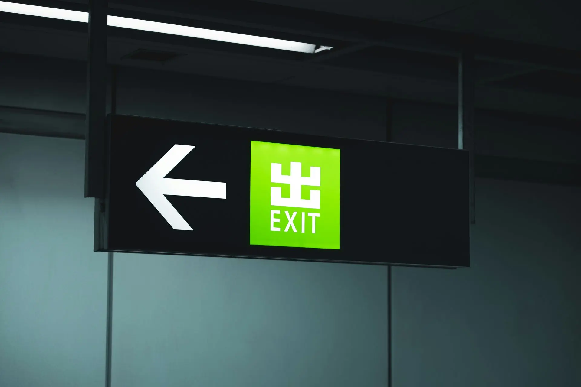 Illuminated Exit Sign with Directional Arrow Illuminated exit sign with a green background and left arrow, prominently displaying the word "EXIT."
